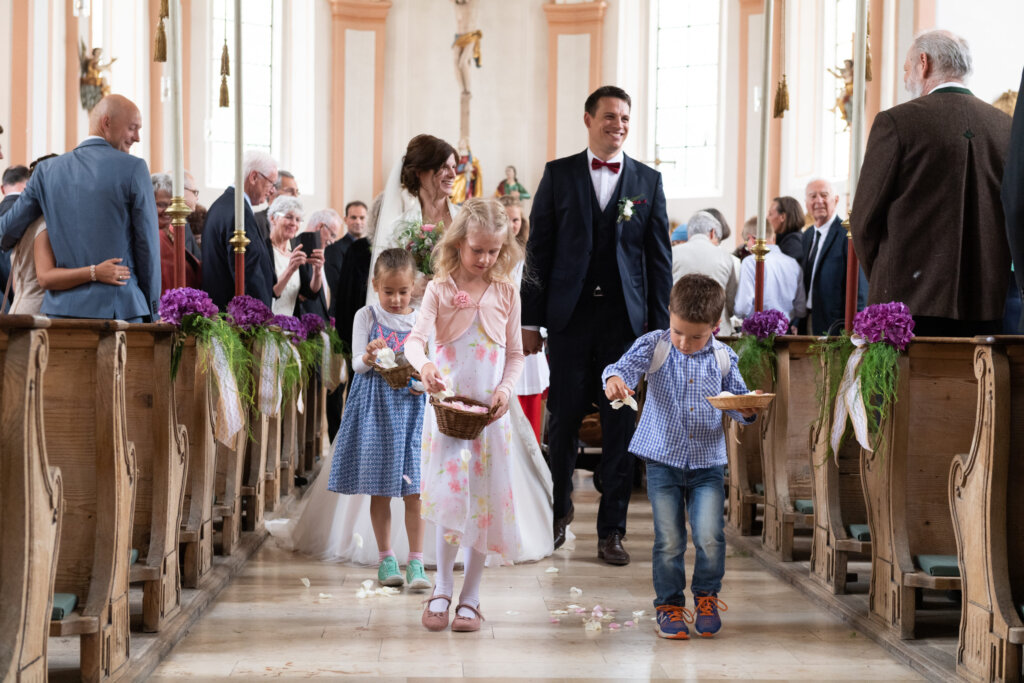 Hochzeitsfotografie: Ein Brautpaar und Kinder gehen durch den Mittelgang einer Kirche