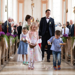 Hochzeitsfotografie: Ein Brautpaar und Kinder gehen durch den Mittelgang einer Kirche